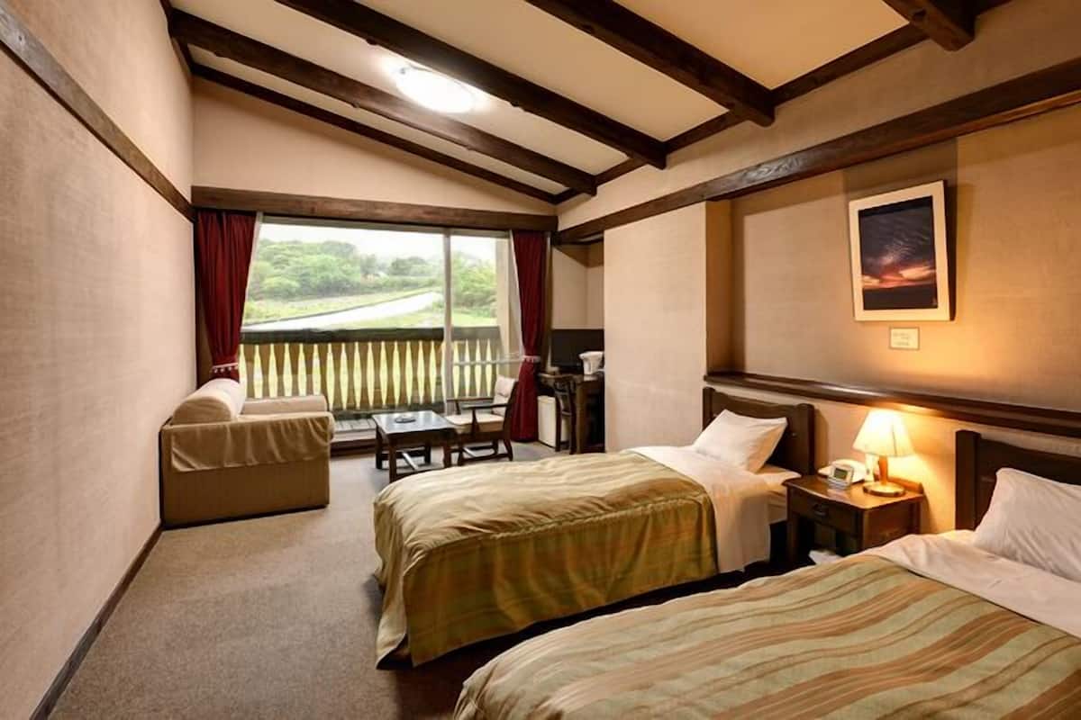 Ein Hotelzimmer mit zwei Betten, einem kleinen Tisch, einem Stuhl, einem Fenster mit Blick und einem Bild an der Wand.