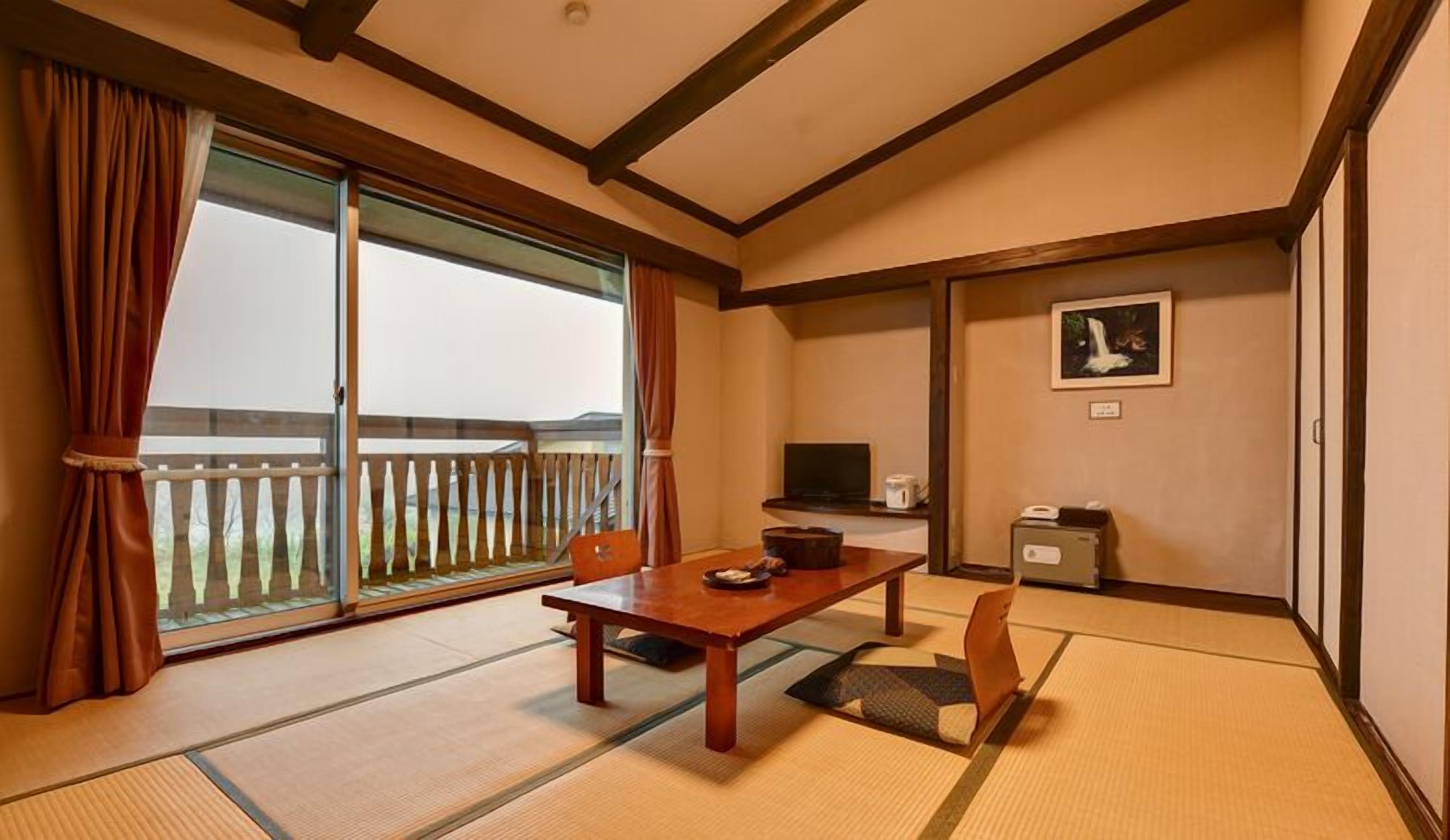 A traditional Japanese room with tatami flooring, a sliding door to a balcony, a television, and a framed picture on the wall.