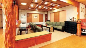 A traditional Japanese-style living room with tatami flooring, low wooden furniture, and a large wooden tree trunk. - Echigoya Ryokan <miyagiken> (Osaki)