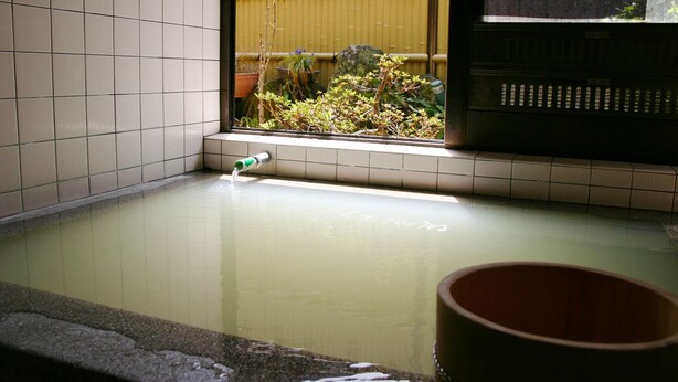 A hot spring area with a tiled wall, a small water feature, and a view of plants and a bamboo fence.