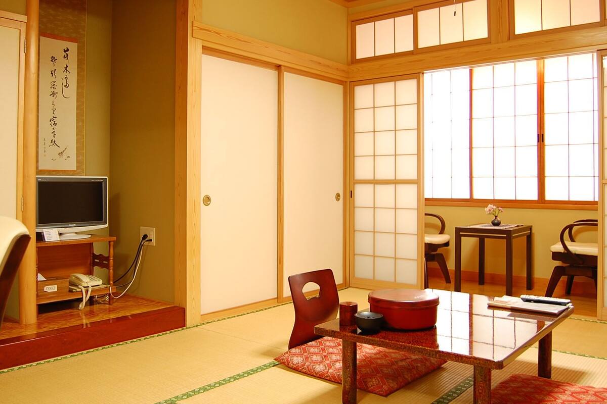 A traditional Japanese room with tatami flooring, a low table with a red mat, a television, and a shoji screen door.