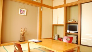 A traditional Japanese-style room with tatami flooring, a wooden table, a red chair, a television, and a small cabinet.