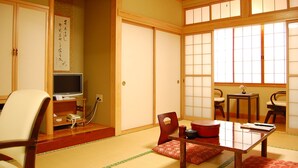 A traditional Japanese room with tatami flooring, a low table with a red mat, a television, and a shoji screen door.