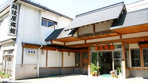 A building with a sign reading '越後屋' and a covered entrance area with potted plants.