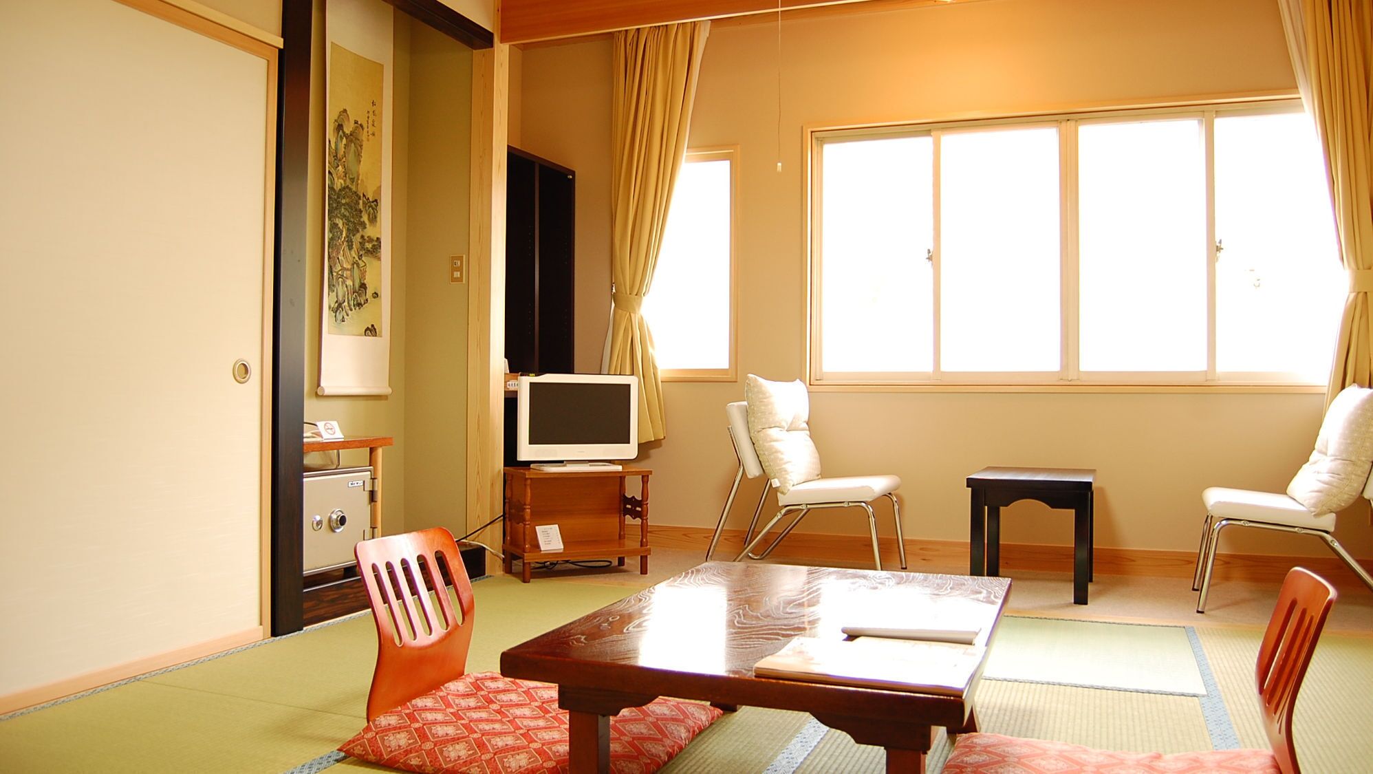 Una habitación tradicional japonesa con suelo de tatami, televisor, escritorio y dos sillas.