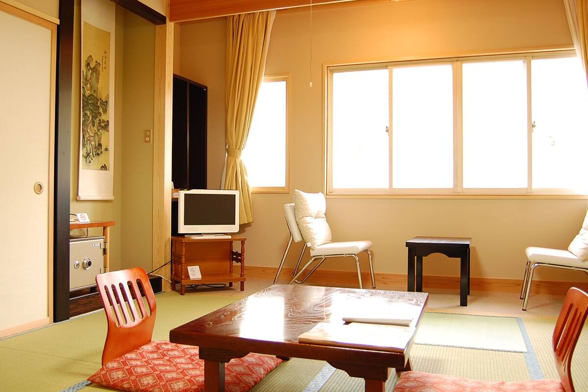 A traditional Japanese room with tatami flooring, a television, a desk, and a chair.