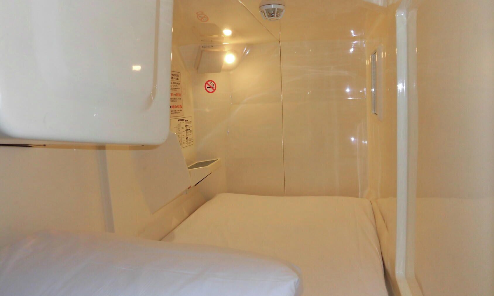 A small, enclosed room with a bed, a control panel, and a no-smoking sign.