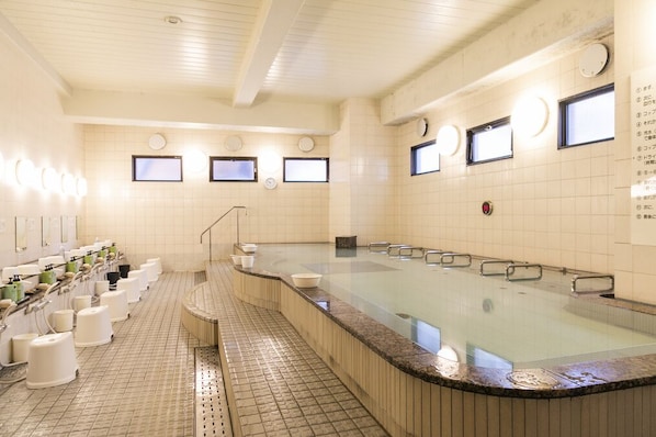 A public bath area with multiple sinks, a large central hot tub, and tiled walls.