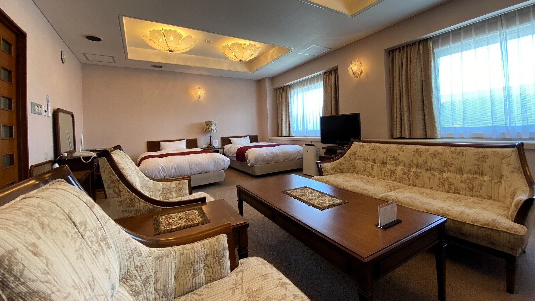 A hotel room with two beds, a sofa, a coffee table, and a television.