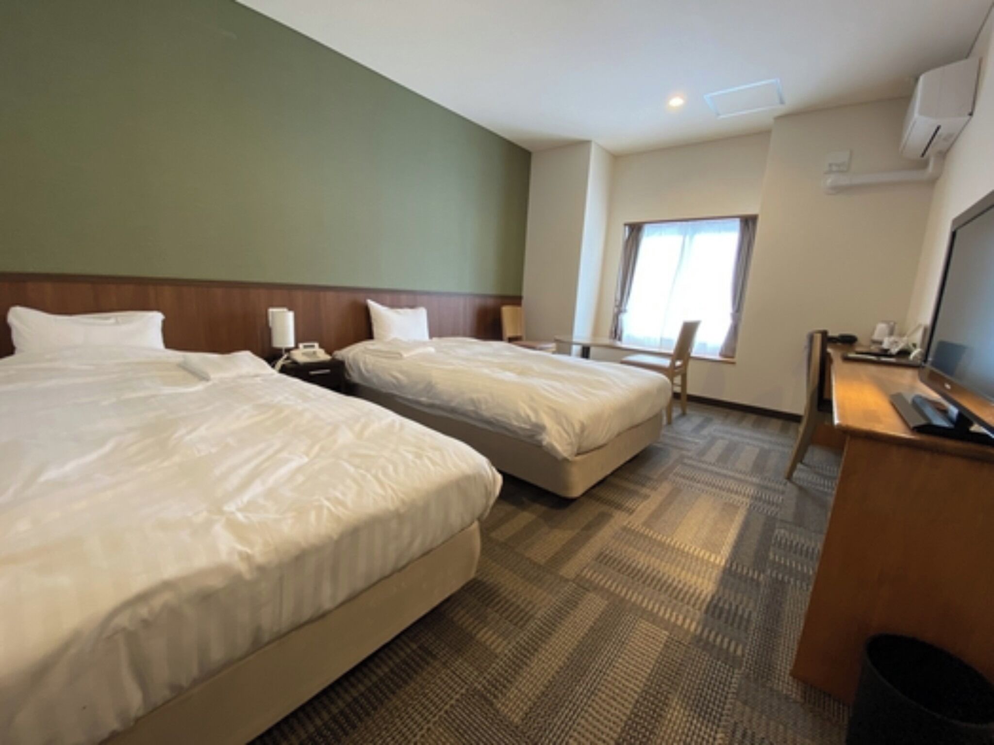 A hotel room with two beds, a desk, a chair, a TV, and a window.