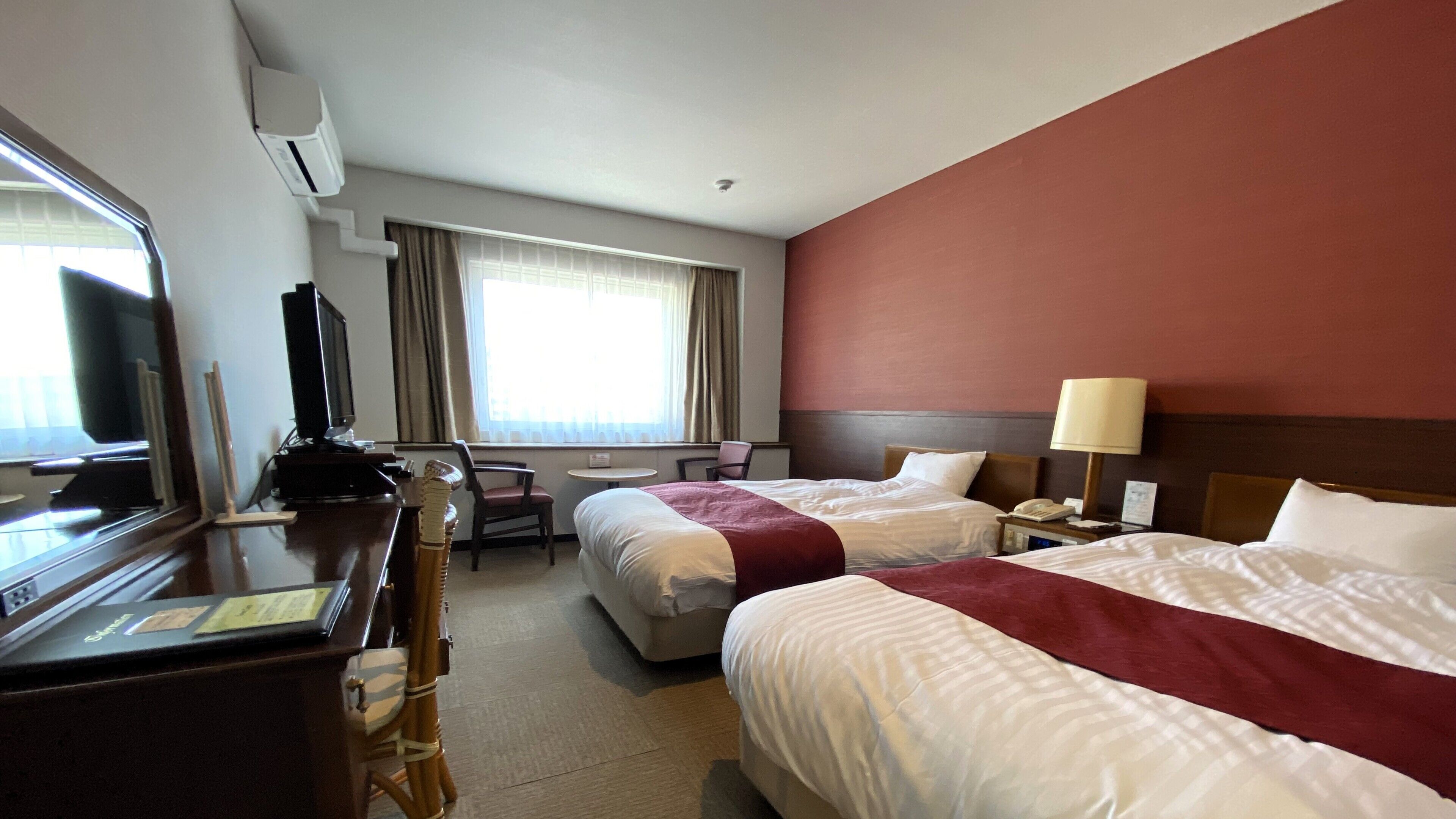 A hotel room with two beds, a desk, a television, a chair, and a window with curtains.