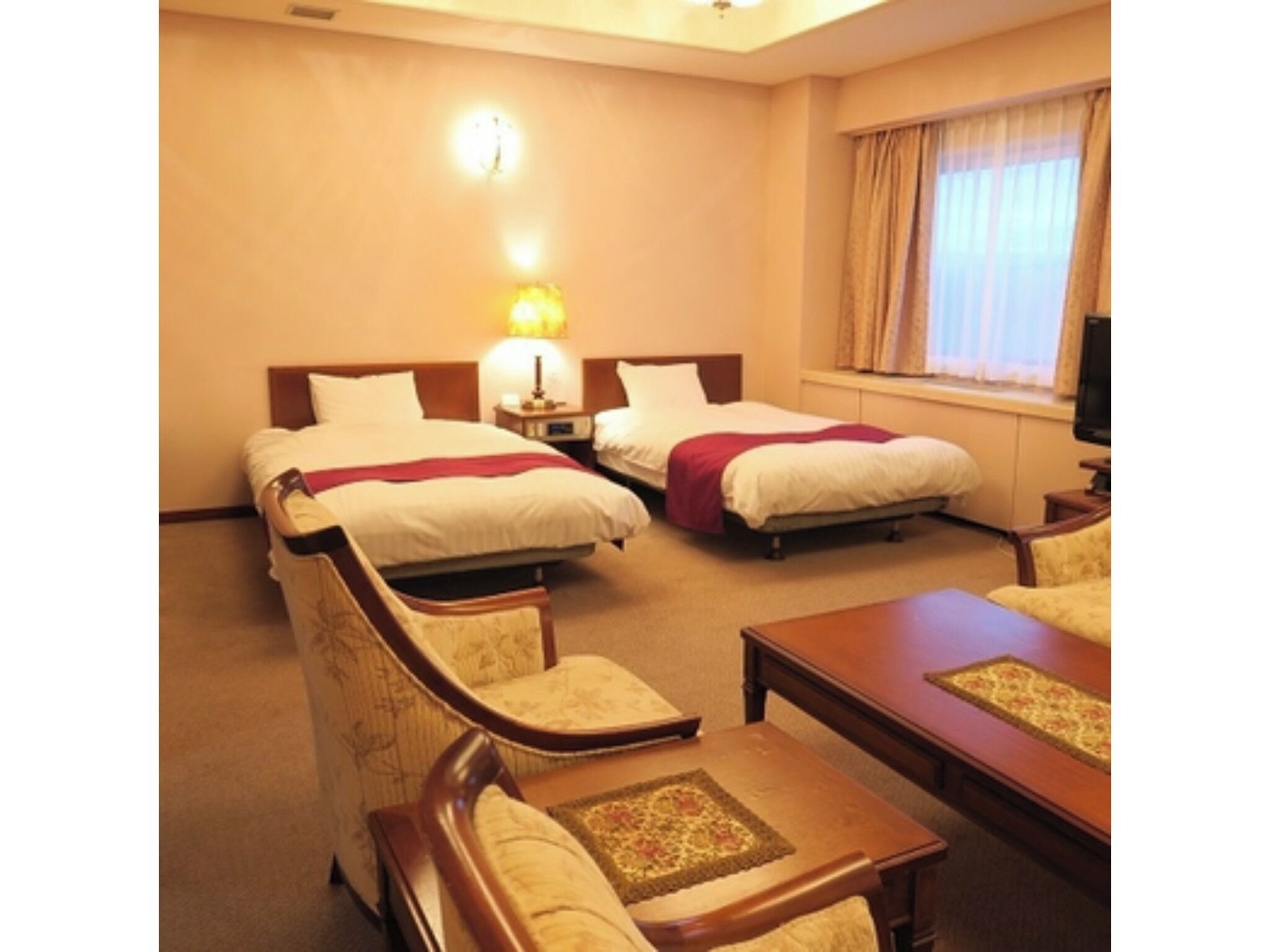 A hotel room with two beds, a sofa, a table, a lamp, and a television.