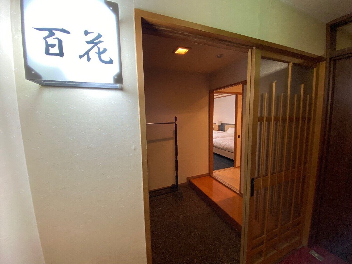 A hotel room with a bed, a wooden sliding door, and a sign with Japanese characters.