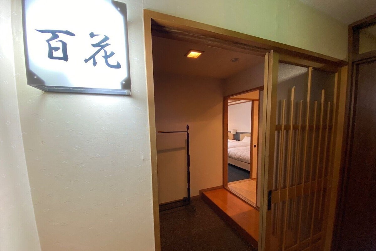 A hotel room with a bed, a wooden sliding door, and a sign with Japanese characters.