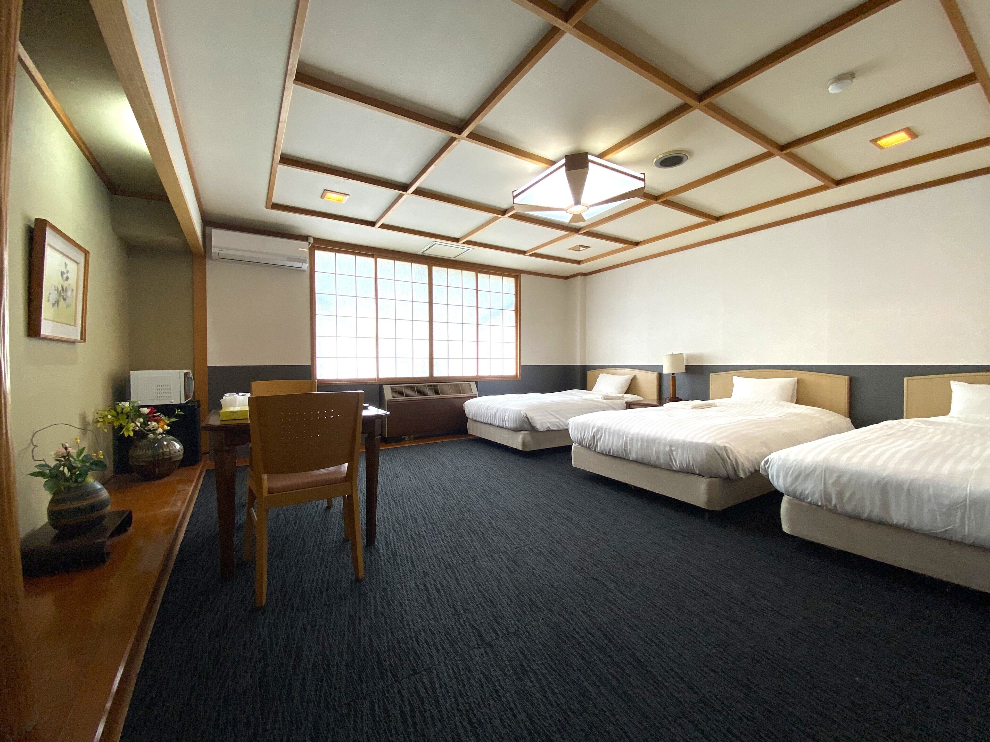 A hotel room with a desk, two beds, a chair, and a large window.