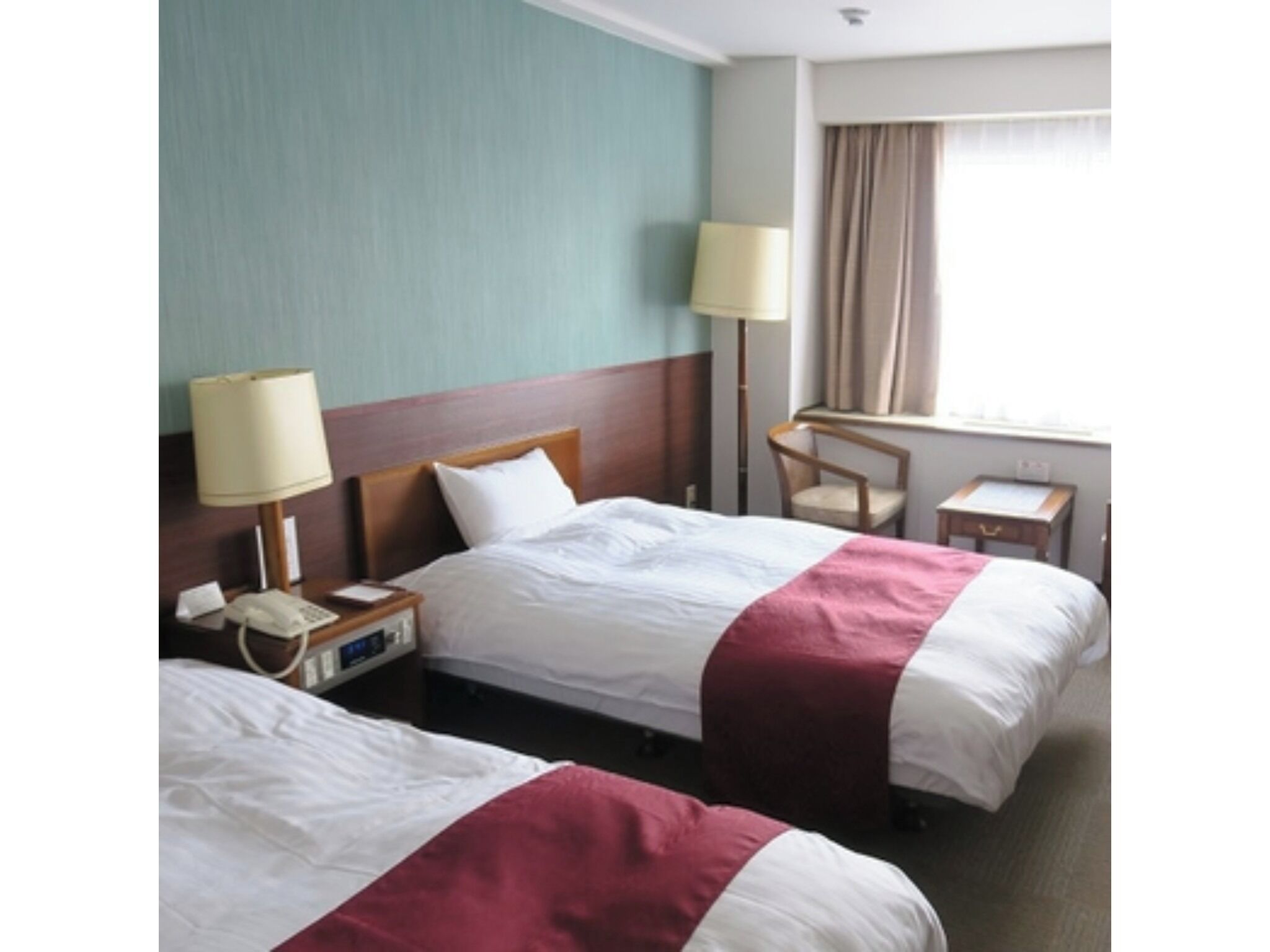 A hotel room with two beds, a desk, a chair, a lamp, and a window with curtains.