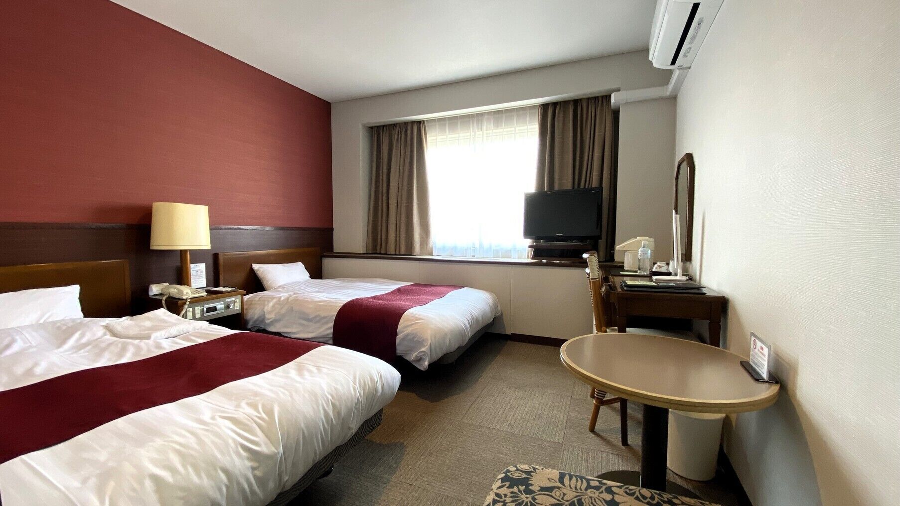 A hotel room with two beds, a TV, a desk, and a bathroom.