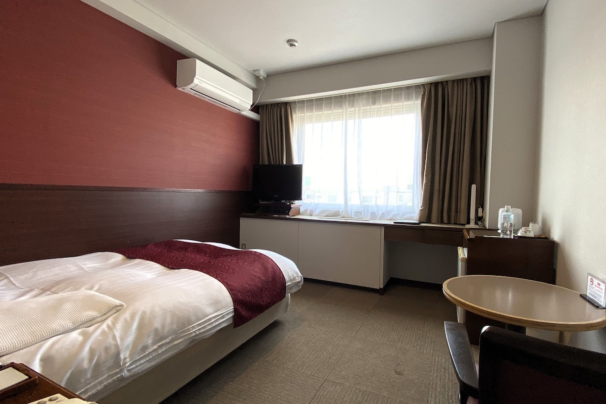 Habitación de hotel con cama, escritorio con silla, televisor y ventana con cortinas.