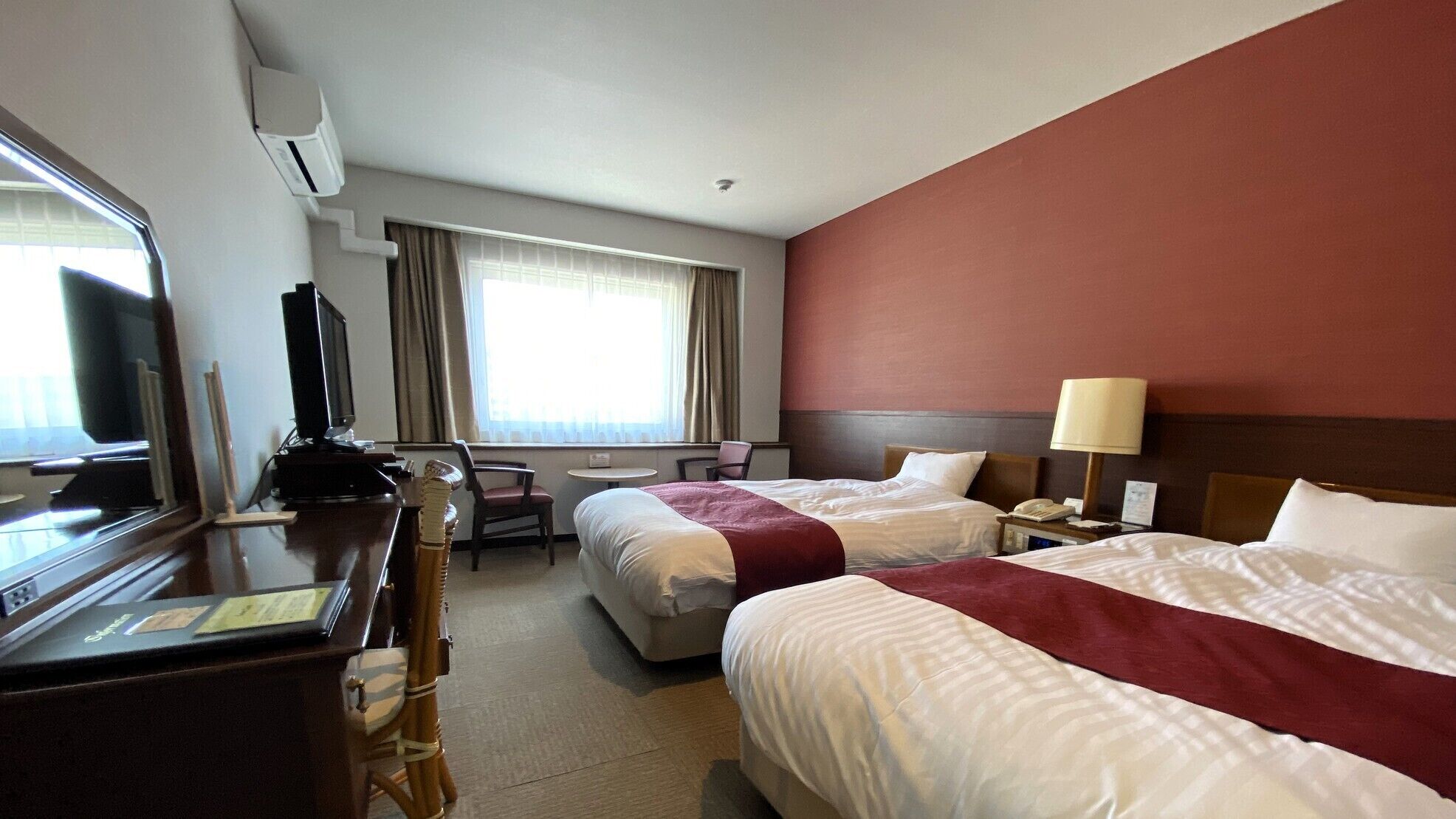 A hotel room with two beds, a desk with a computer, a television, and a window with curtains.