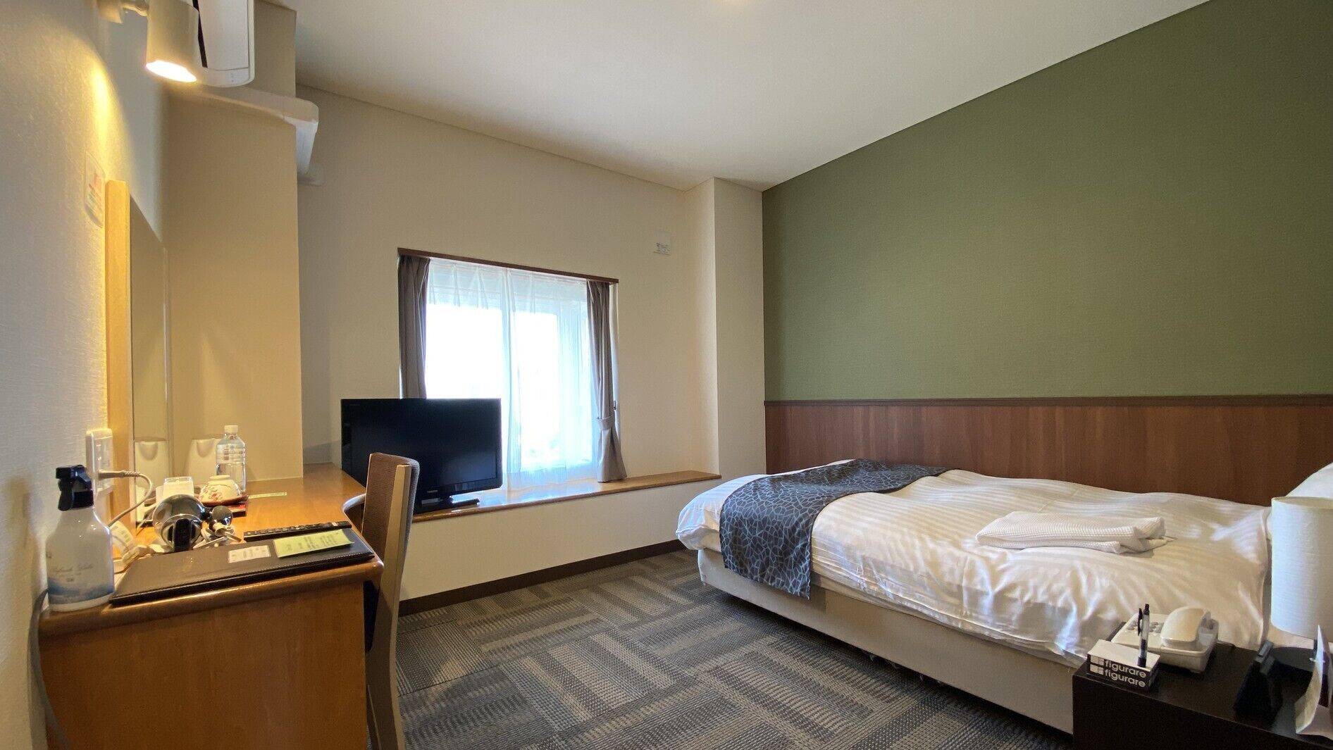 A hotel room with a bed, a desk with a computer, a television, and a window with curtains.