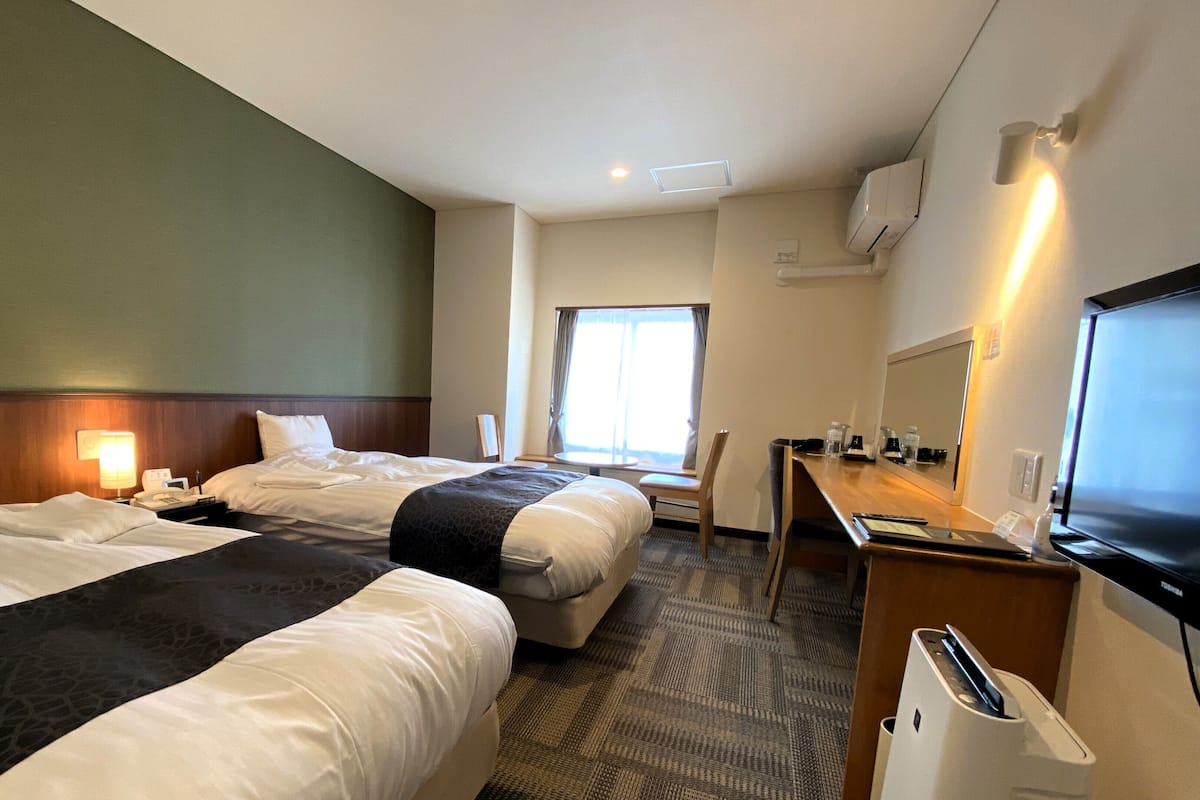 A hotel room with two beds, a desk, a television, and a window.