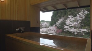 Une baignoire en bois donnant sur des cerisiers en fleurs, vue à travers une fenêtre.