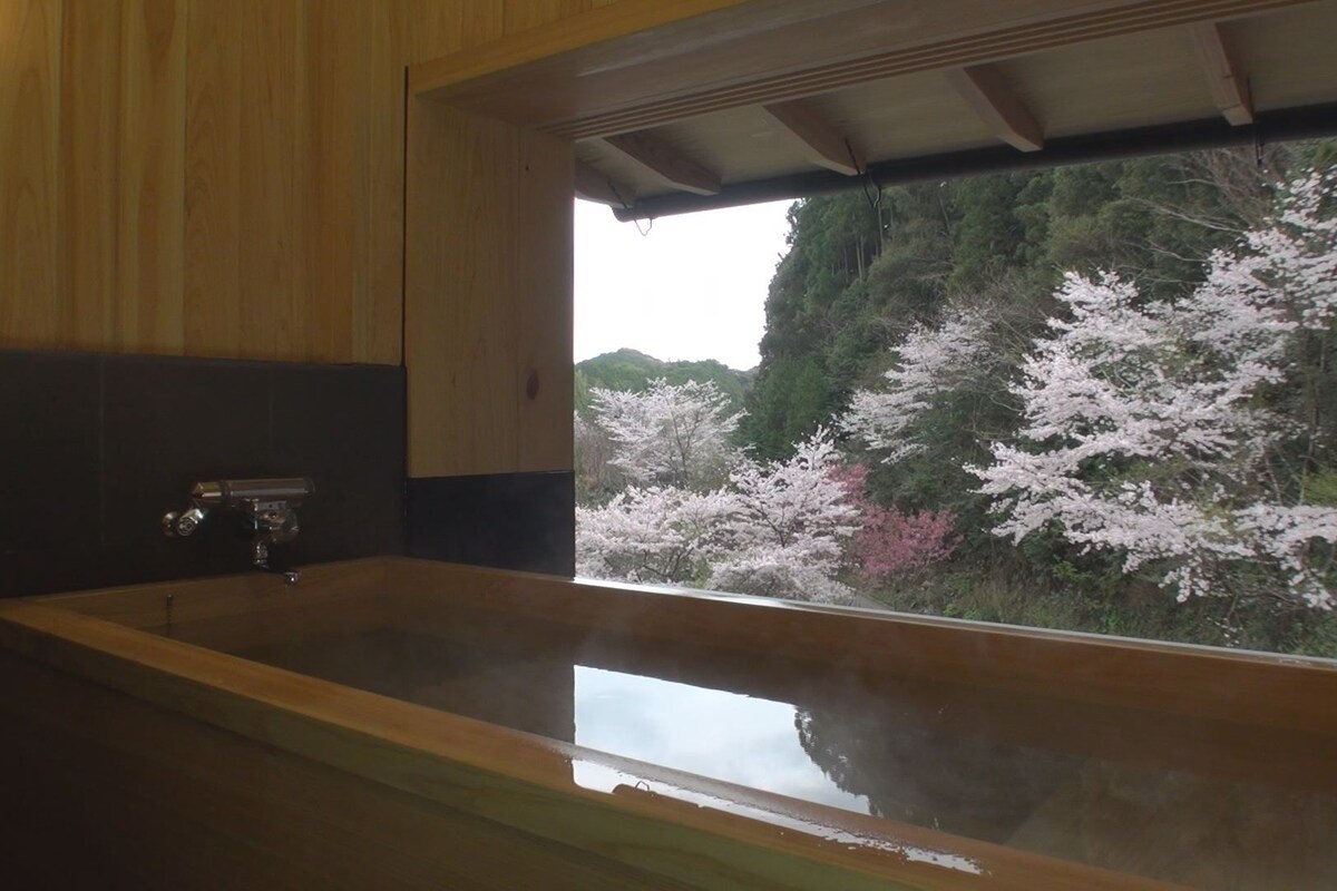 A bathroom with a wooden vanity, a sink, and a window with a view of cherry blossoms.