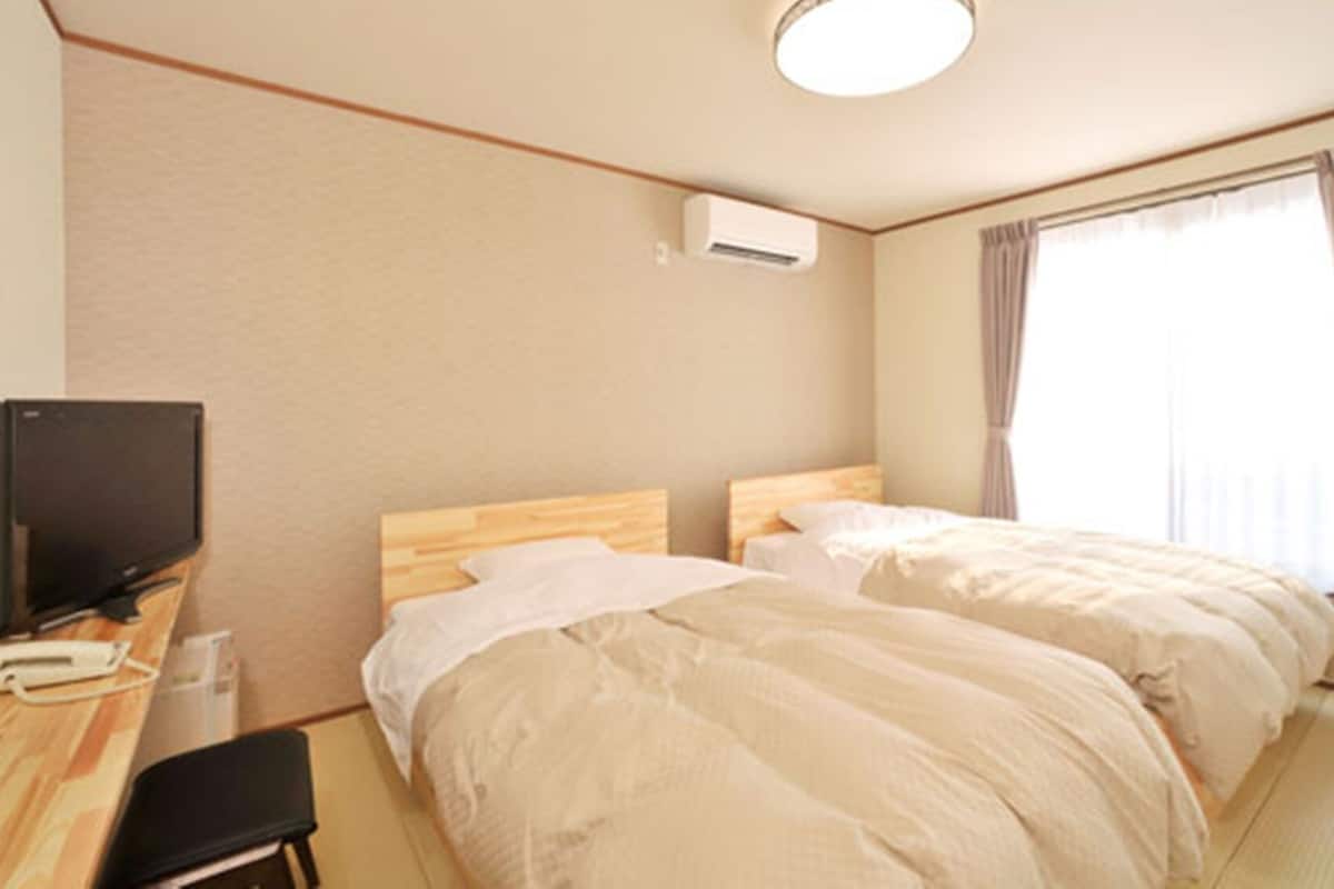 Ein Hotelzimmer mit zwei Betten, einem Schreibtisch mit Fernseher und einer Klimaanlage.