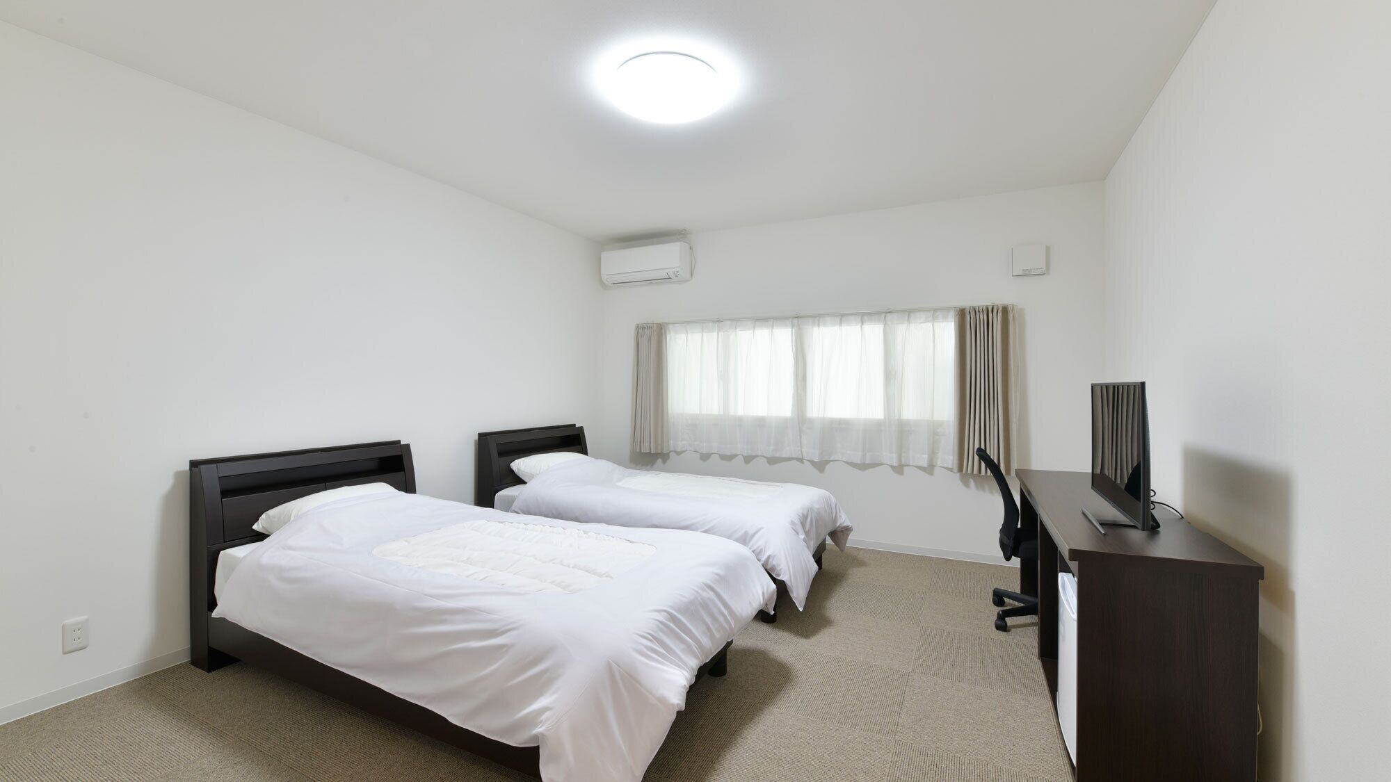 Una habitación de hotel con dos camas, un escritorio, un televisor y una ventana con cortinas.