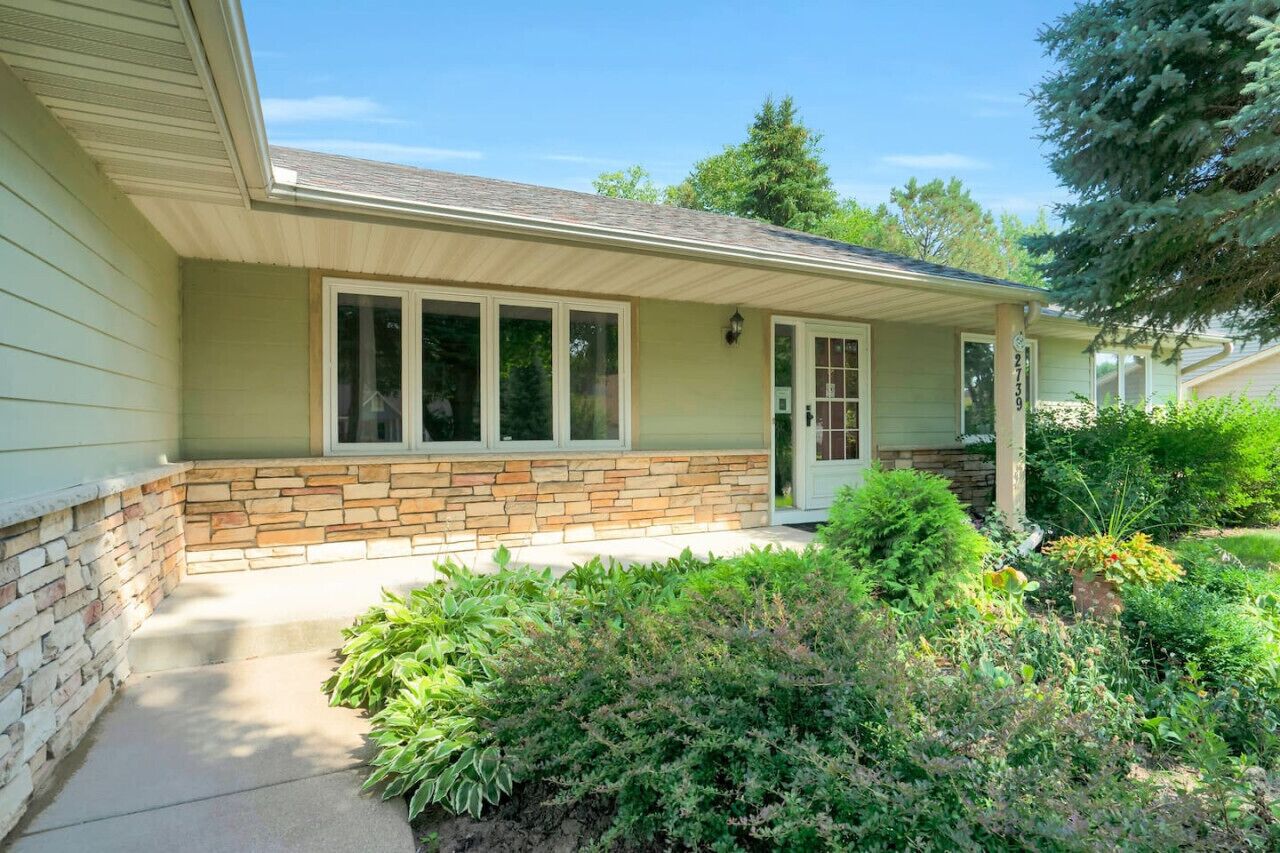 A single-story house with a stone foundation, a front porch, and a well-maintained garden.