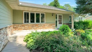 Une maison de plain-pied avec des fondations en pierre, un porche à l’avant et un jardin bien entretenu.