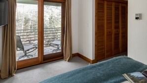A room with a sliding glass door to a balcony, a wooden wardrobe, and a bed with a blue blanket. - Outpost: Windflower 2115 - Mountain Views! (Wilson)