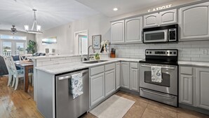 A modern kitchen with white cabinetry, stainless steel appliances, and a view to the dining area.
