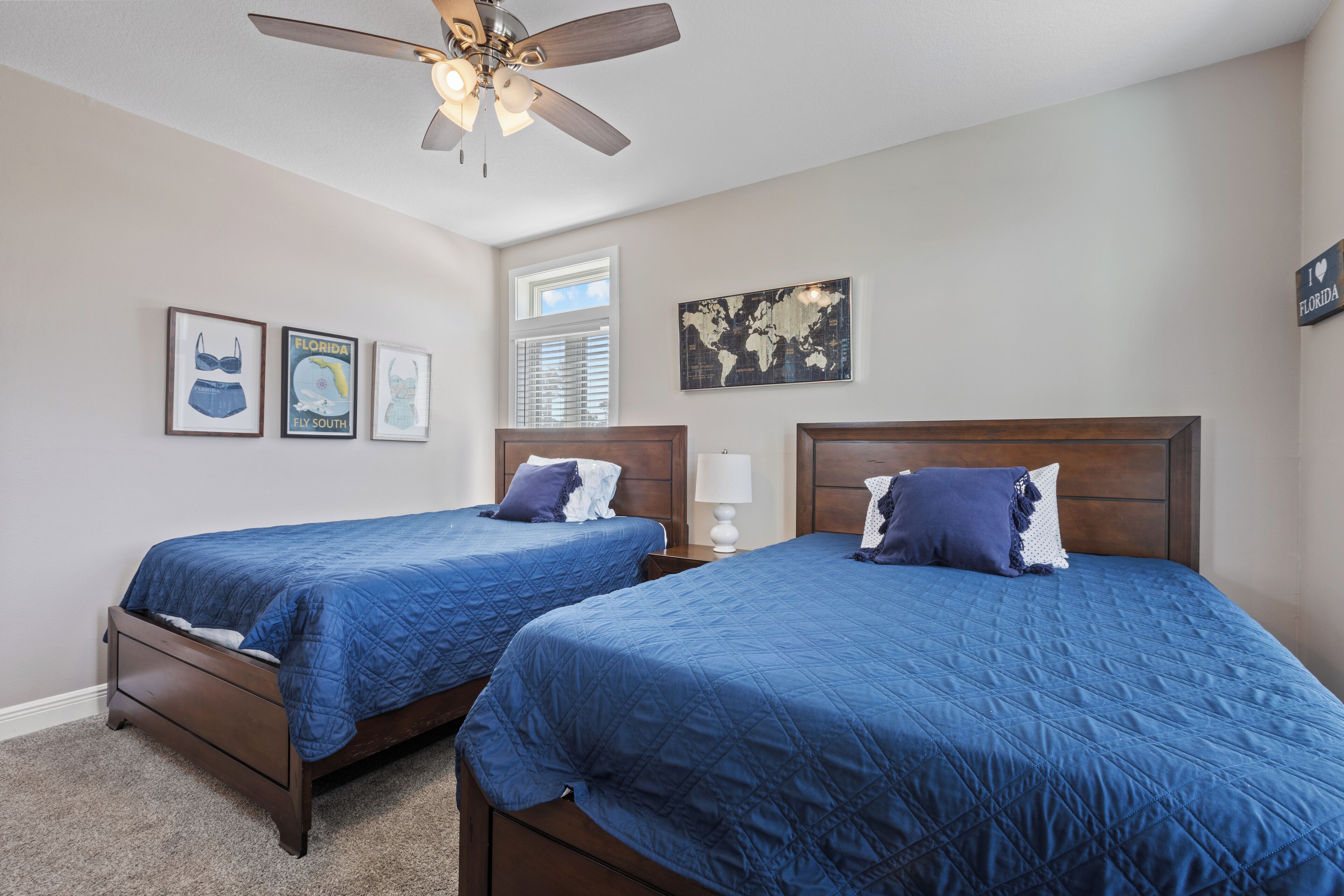 A bedroom with two beds, a ceiling fan, a world map, and framed pictures on the wall.