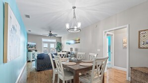 A dining area with a wooden table and white chairs, a chandelier, and a view of a balcony.