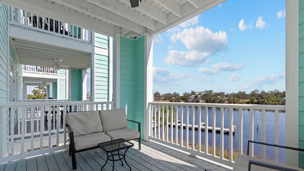 A covered porch with a white railing, a beige sofa, and a view of a body of water.