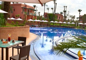 Zona junto a la piscina con una piscina curva, sillones de descanso, sombrillas y una mesa de comedor con una bebida.