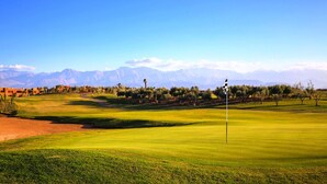Un terrain de golf avec un mât de drapeau au premier plan, un ciel dégagé et des montagnes en arrière-plan.