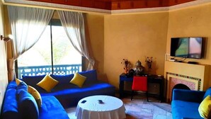 Un salon avec un canapé bleu, une table basse ronde, un téléviseur et une cheminée.