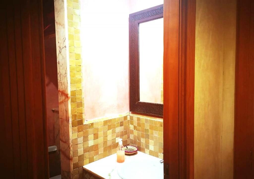 A bathroom with a tiled wall, a window, and a sink with a soap dispenser.