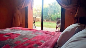 A bedroom with a bed, a red and gray blanket, and a view of an outdoor area with a chair and greenery. - Palmeraie Village 609 (Marrakech)