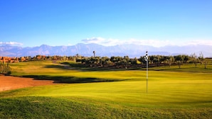 A golf course with a flagstick in the foreground, a clear sky, and mountains in the background. - Palmeraie Village 609 (Marrakech)