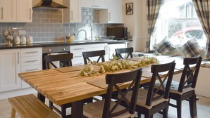 Cozinha moderna com armários brancos, exaustor preto e área de refeições com mesa e cadeiras de madeira.