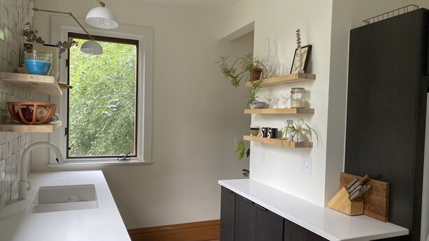 A modern kitchen with a white countertop, dark cabinets, and a window with a view of greenery. - Eclectic Home Near UWM Campus and Lake Michigan (Shorewood)