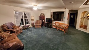 A living room with a brown leather sofa, patterned armchairs, a wooden bench, a television, a lamp, and a bookshelf. - Cottage at Chimney Ridge Farms (Duncansville)