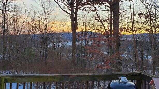 A wooden deck with a view of a forest and a body of water during sunset. - Cottage at Chimney Ridge Farms (Duncansville)