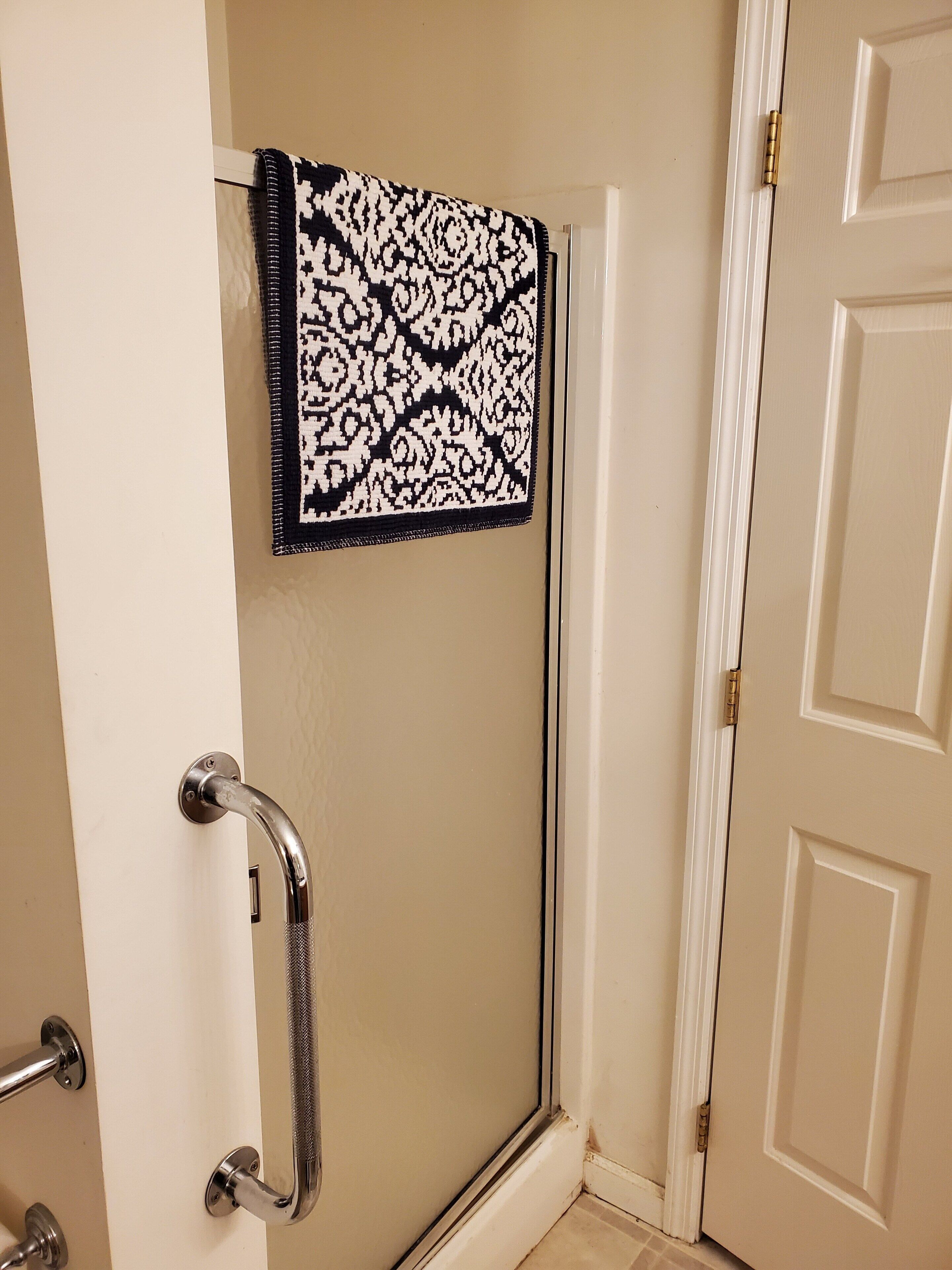 A bathroom with a shower door, a towel rack with a patterned towel, and a door with a brass handle.