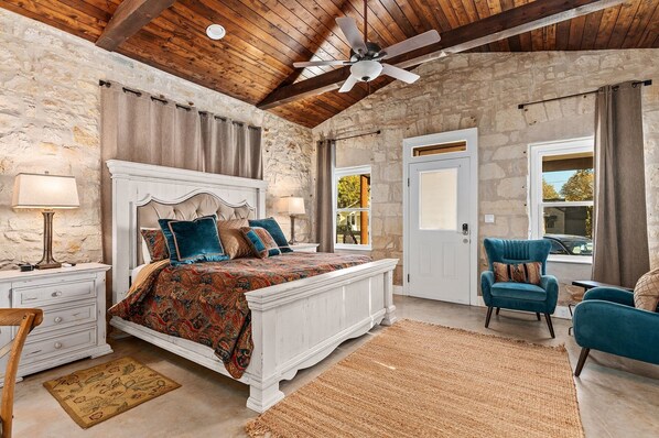 Quarto com uma cama grande, ventilador de teto, paredes de pedra e vista para o exterior.