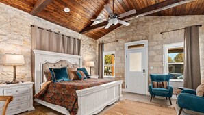 Una camera da letto con un letto grande, un ventilatore a soffitto, pareti in pietra e vista all'esterno.