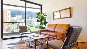 Ein modernes Wohnzimmer mit Ledersofa, Couchtisch und Sessel. Ein großes Fenster bietet Blick auf Gebäude und Berge.